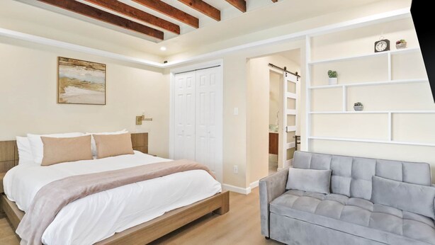 A bedroom with a bed, a grey sofa, a white wardrobe, and a painting on the wall. - Northgate Apartment - 1 block to TAMU! (College Station)