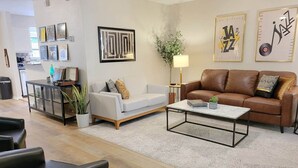 A living room with a sofa, a coffee table, and a brown leather couch. There are framed pictures on the wall and a plant on the coffee table. - Jazz Houzz @ Aggieland (College Station)