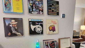 A wall with various framed posters and a black console table with a lava lamp, books, and a record player. - Jazz Houzz @ Aggieland (College Station)