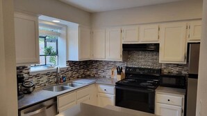 A modern kitchen with white cabinets, a black stove, and a tiled backsplash. - Jazz Houzz @ Aggieland (College Station)
