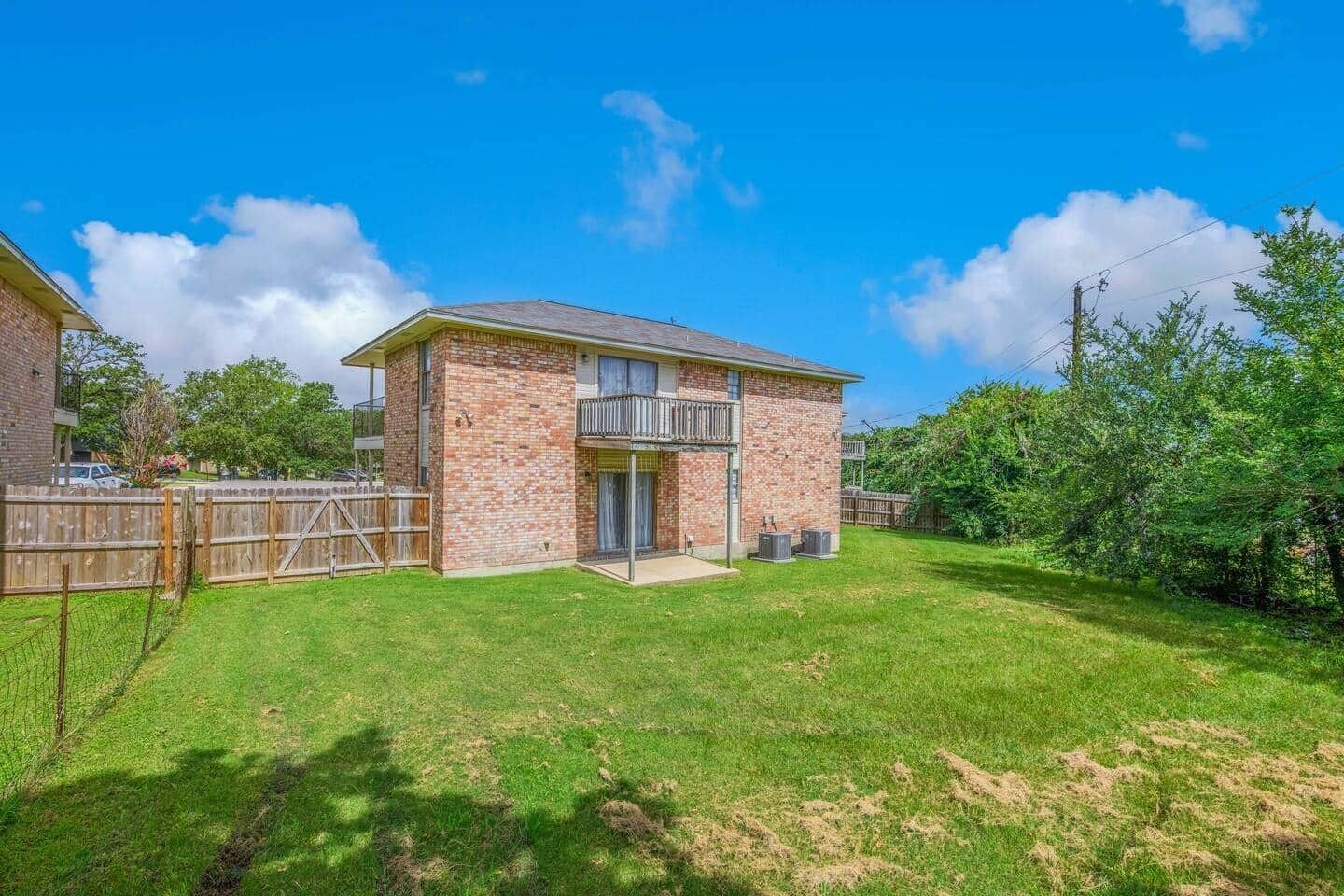A two-story brick house with a balcony, a fenced backyard, and a clear blue sky.