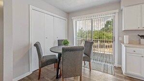 Un comedor con una mesa redonda y cuatro sillas, una planta pequeña en maceta y vistas a una terraza exterior a través de una puerta corrediza de vidrio.