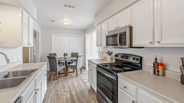 Una cocina moderna con muebles blancos, un comedor con una mesa redonda y sillas, además de un horno y un microondas integrados.