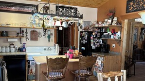 A rustic kitchen with wooden beams, a hanging light fixture, and a refrigerator adorned with photos and magnets.