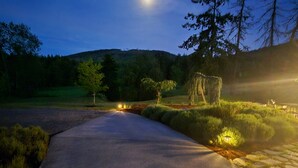 Un sentier pavé mène à un belvédère, qui est entouré d’arbres et dont l’arrière-plan est dominé par une colline.