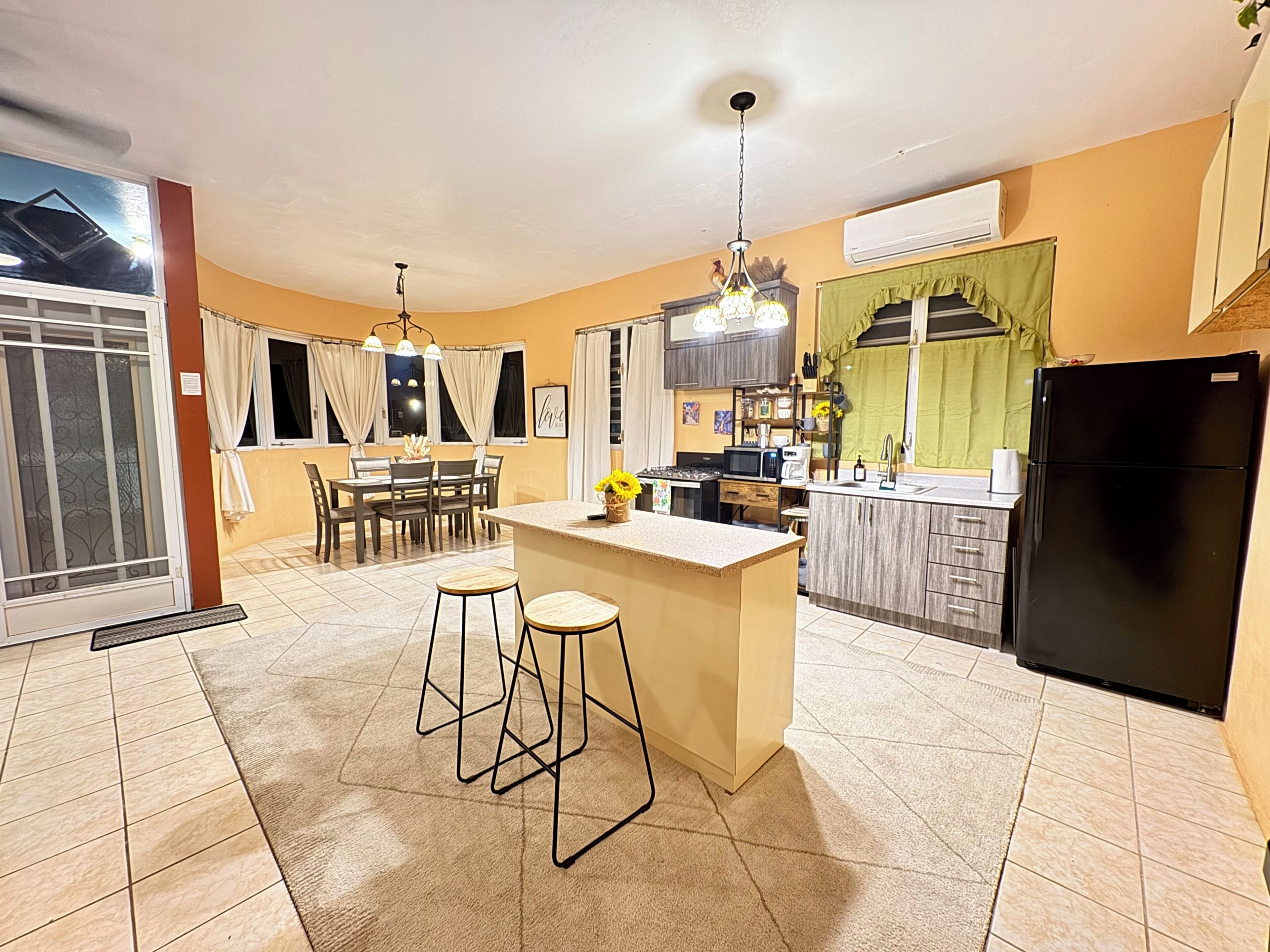 A modern kitchen with a dining area, a black refrigerator, and a window with curtains.