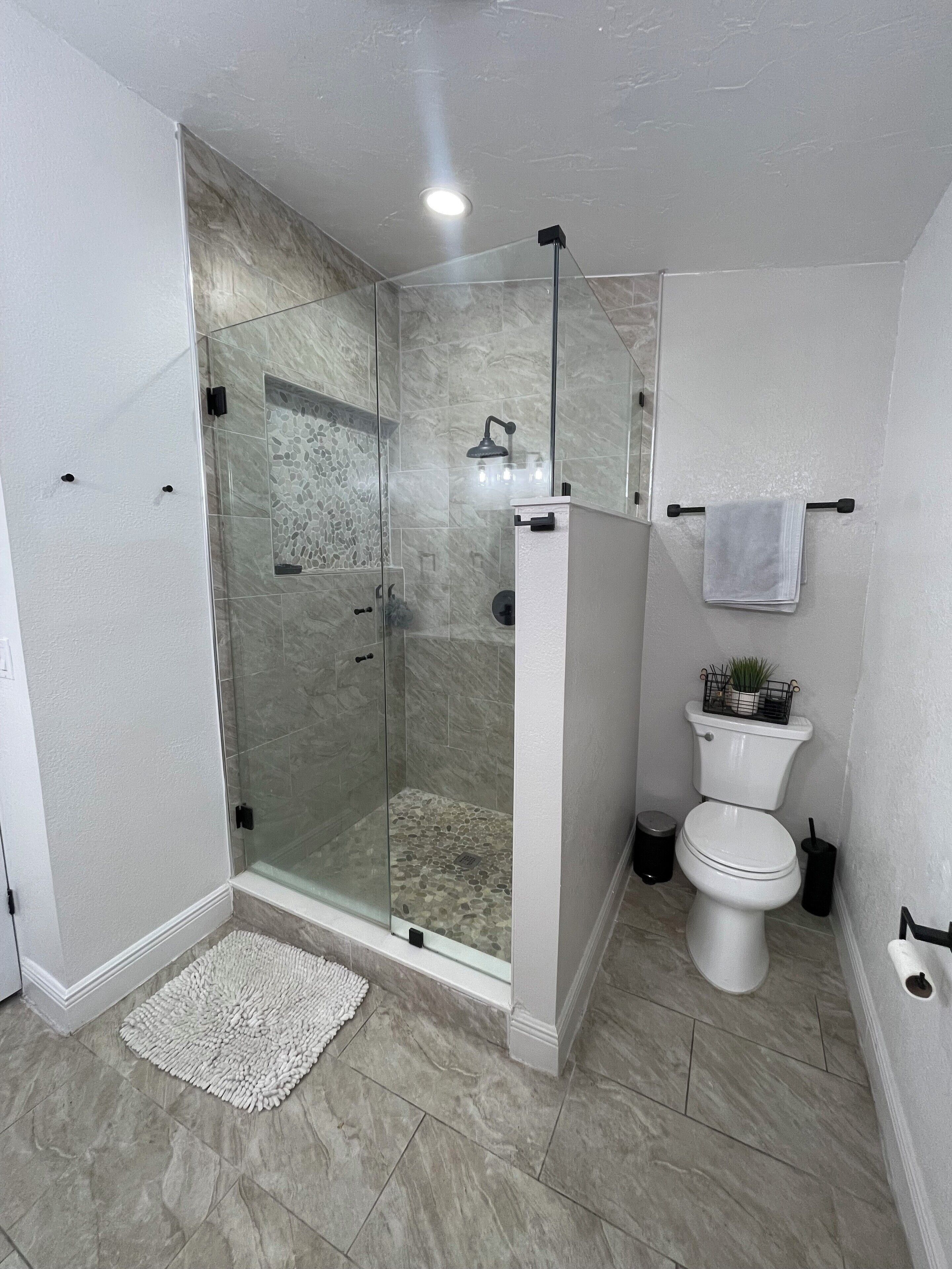 A modern bathroom with a glass-enclosed shower, a toilet, and a sink.