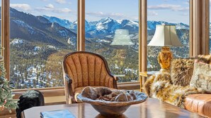 Een kamer met een groot raam met uitzicht op de bergen, een comfortabele fauteuil, een bont plaid en een decoratieve lamp.