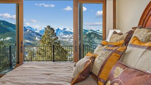 Een slaapkamer met een groot bed, meerdere kussens en uitzicht op besneeuwde bergen vanaf een balkon.