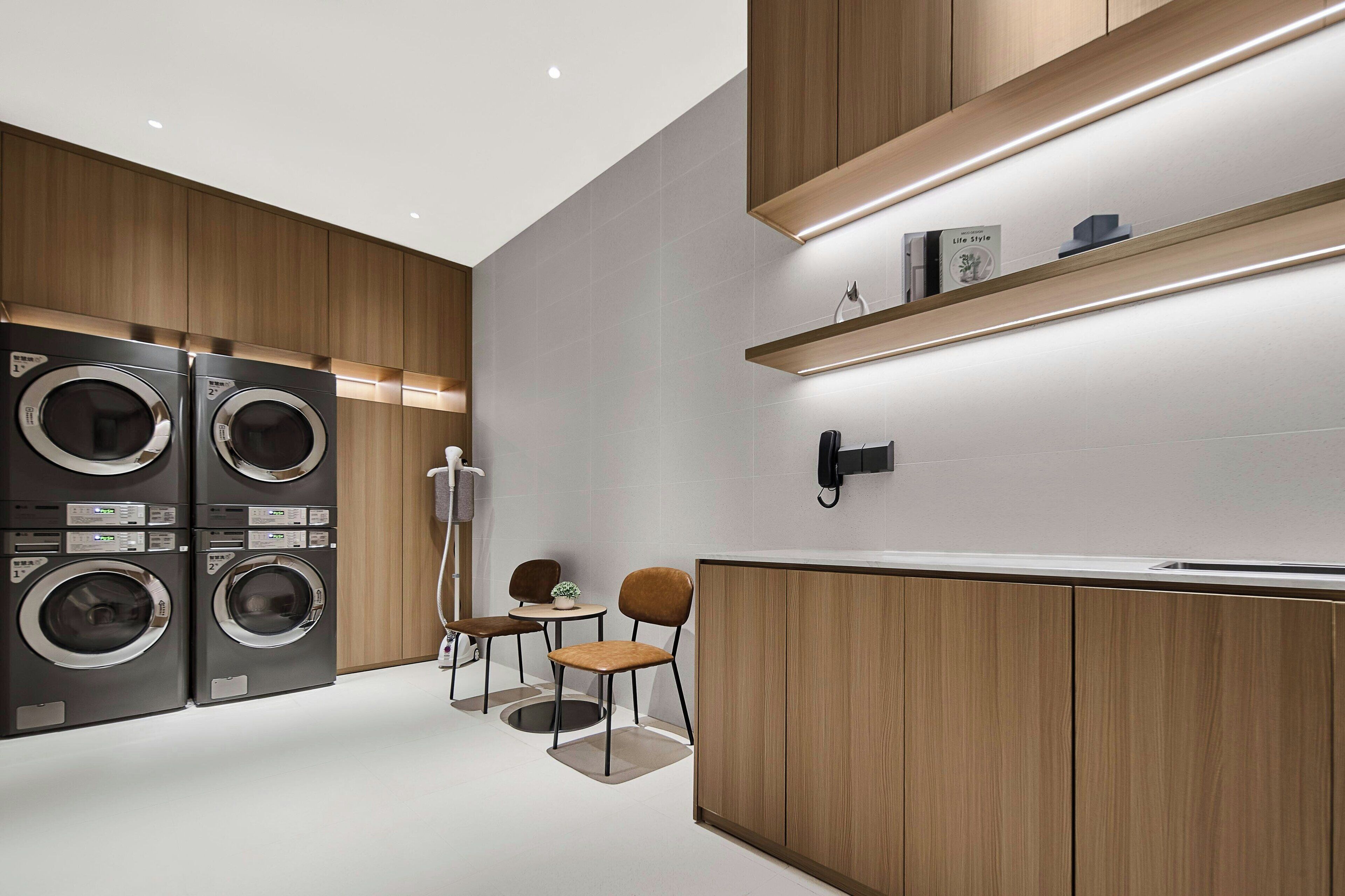 A modern laundry room with built-in washers and dryers, wooden cabinets, and a small seating area with chairs and a table.