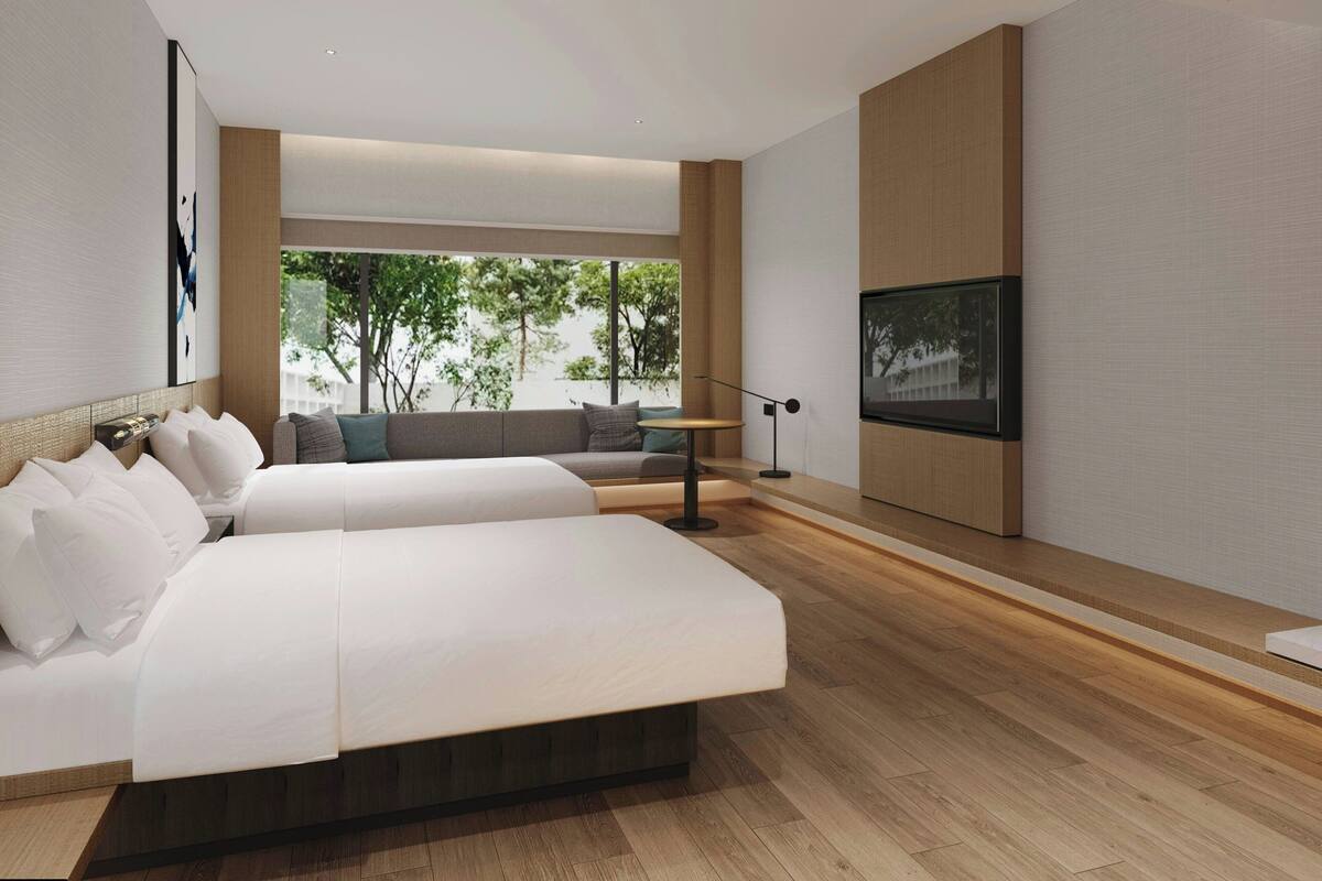Ein modernes Schlafzimmer mit einem großen Bett, einer Couch, einem Fernseher und Blick auf Bäume durch das Fenster.