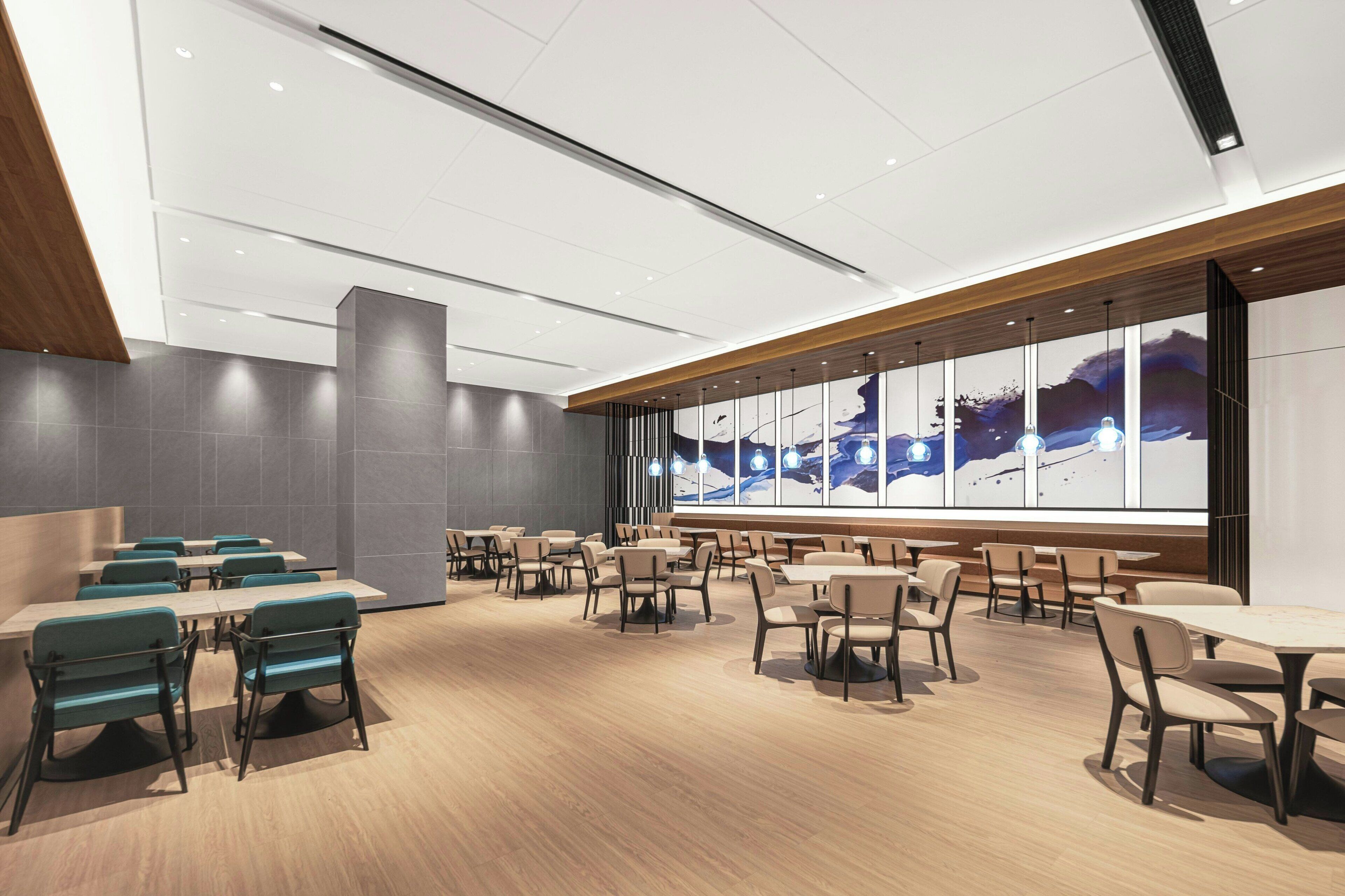 A modern dining area with multiple tables and chairs, large windows with a view, and a wooden ceiling.