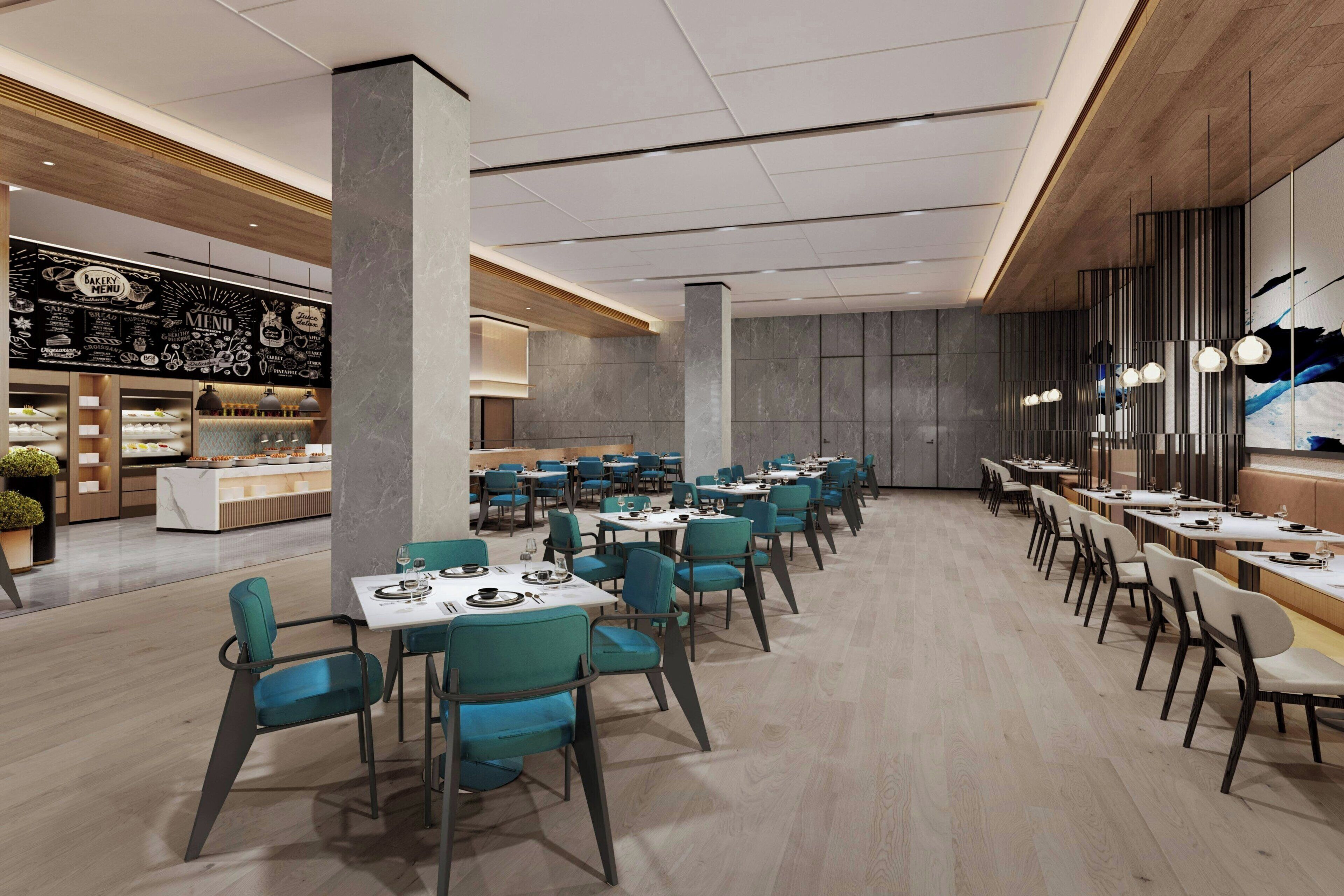 A spacious restaurant with teal chairs and white tables, featuring a blackboard menu and a modern interior design.