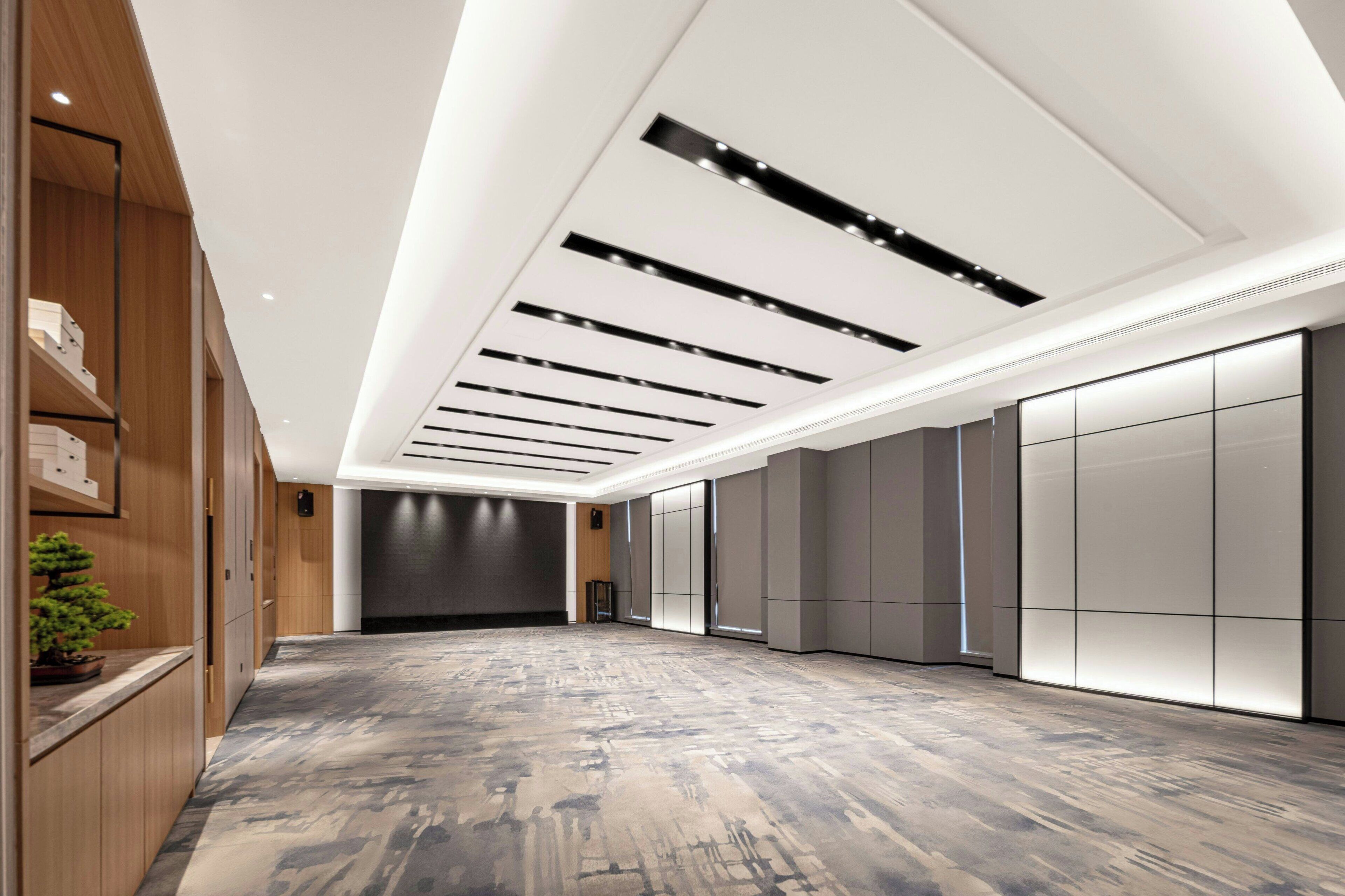 A spacious hotel lobby with a modern design, featuring a wooden reception desk, a large seating area, and a high ceiling with recessed lighting.