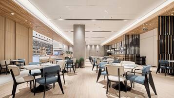 A spacious, modern dining area with multiple tables and chairs, a central pillar, and a kitchen area in the background.