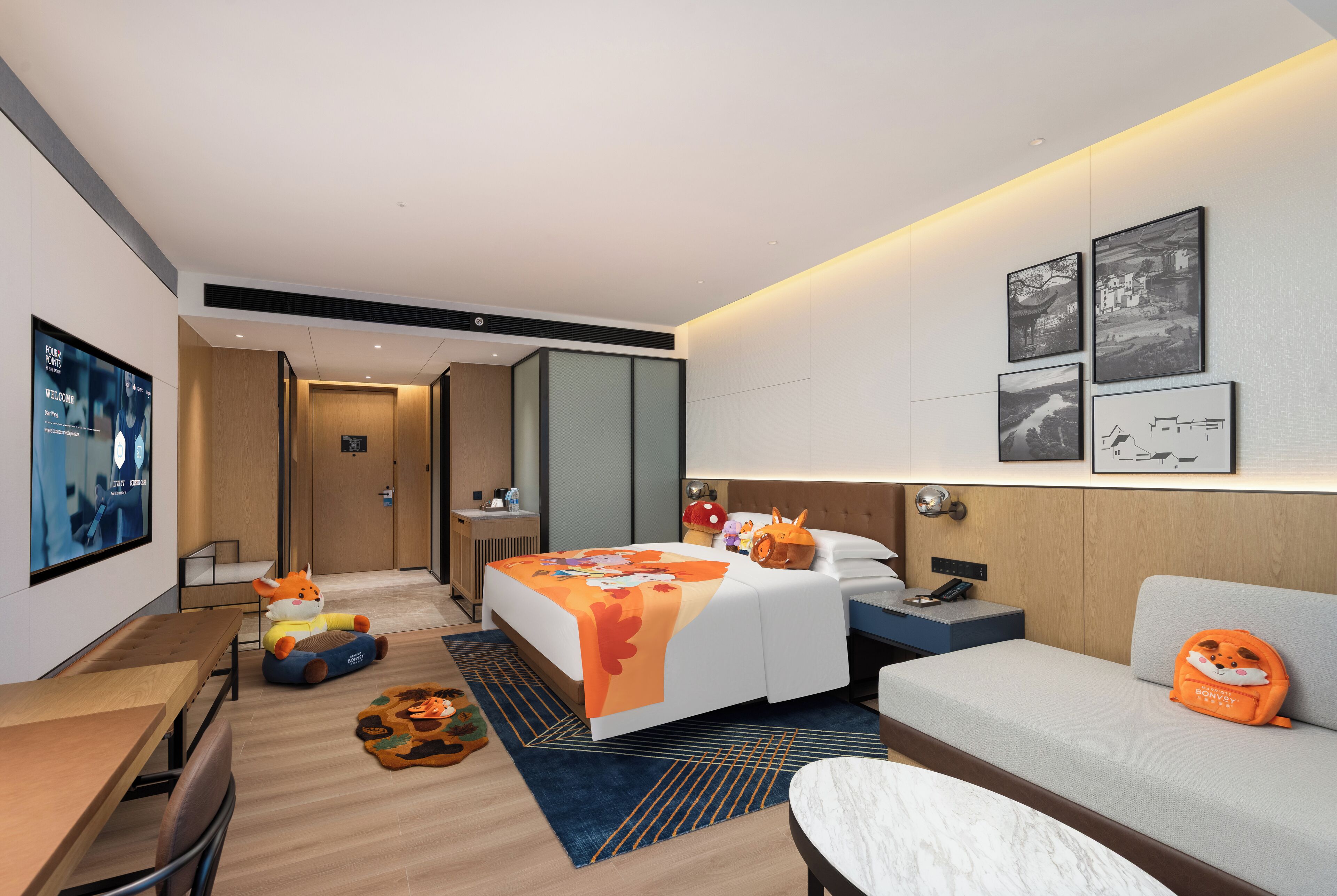 Una moderna camera d'albergo con un letto, un divano, una scrivania e opere d'arte alle pareti.
