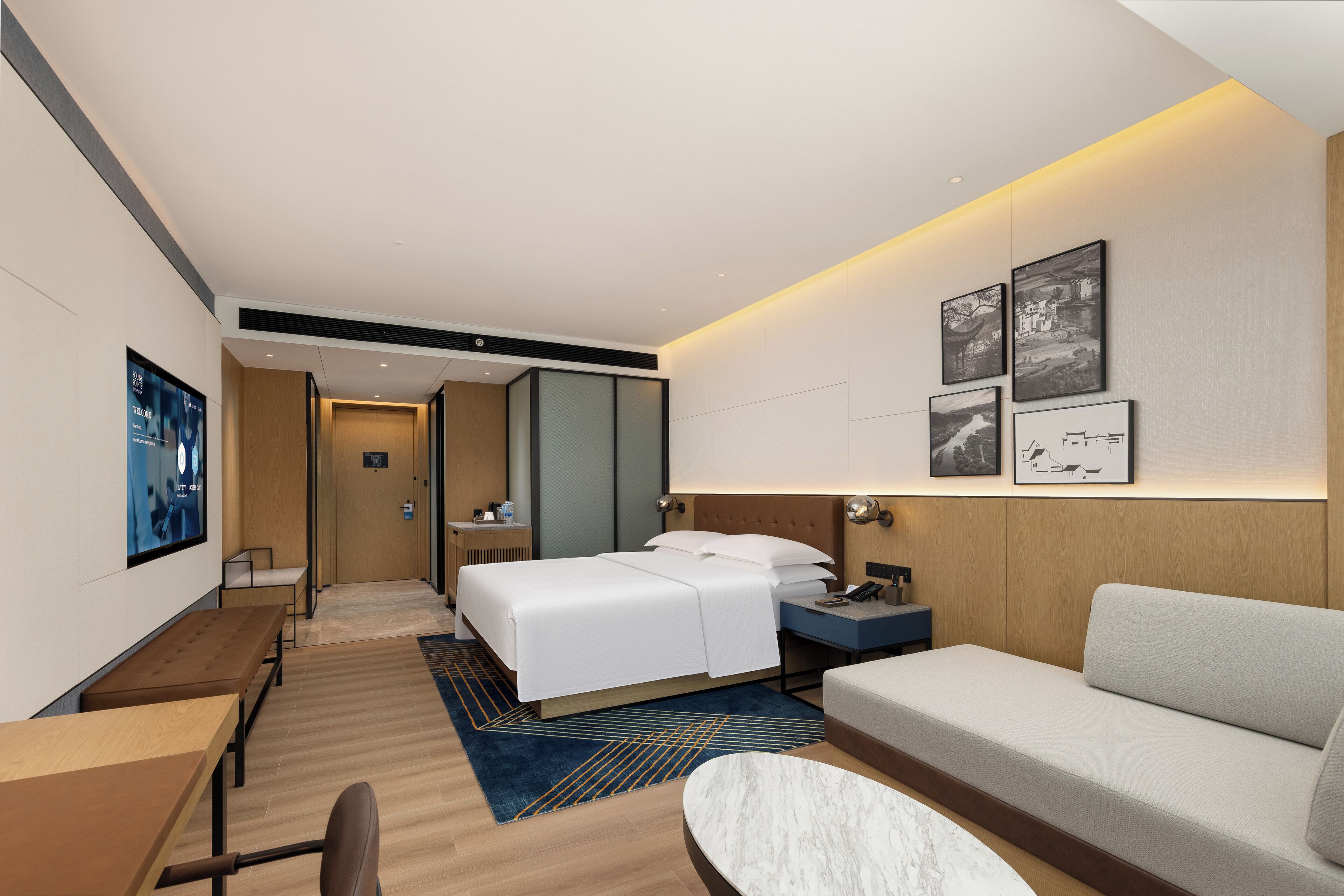 A modern hotel room with a bed, a sofa, a desk, and a bathroom.