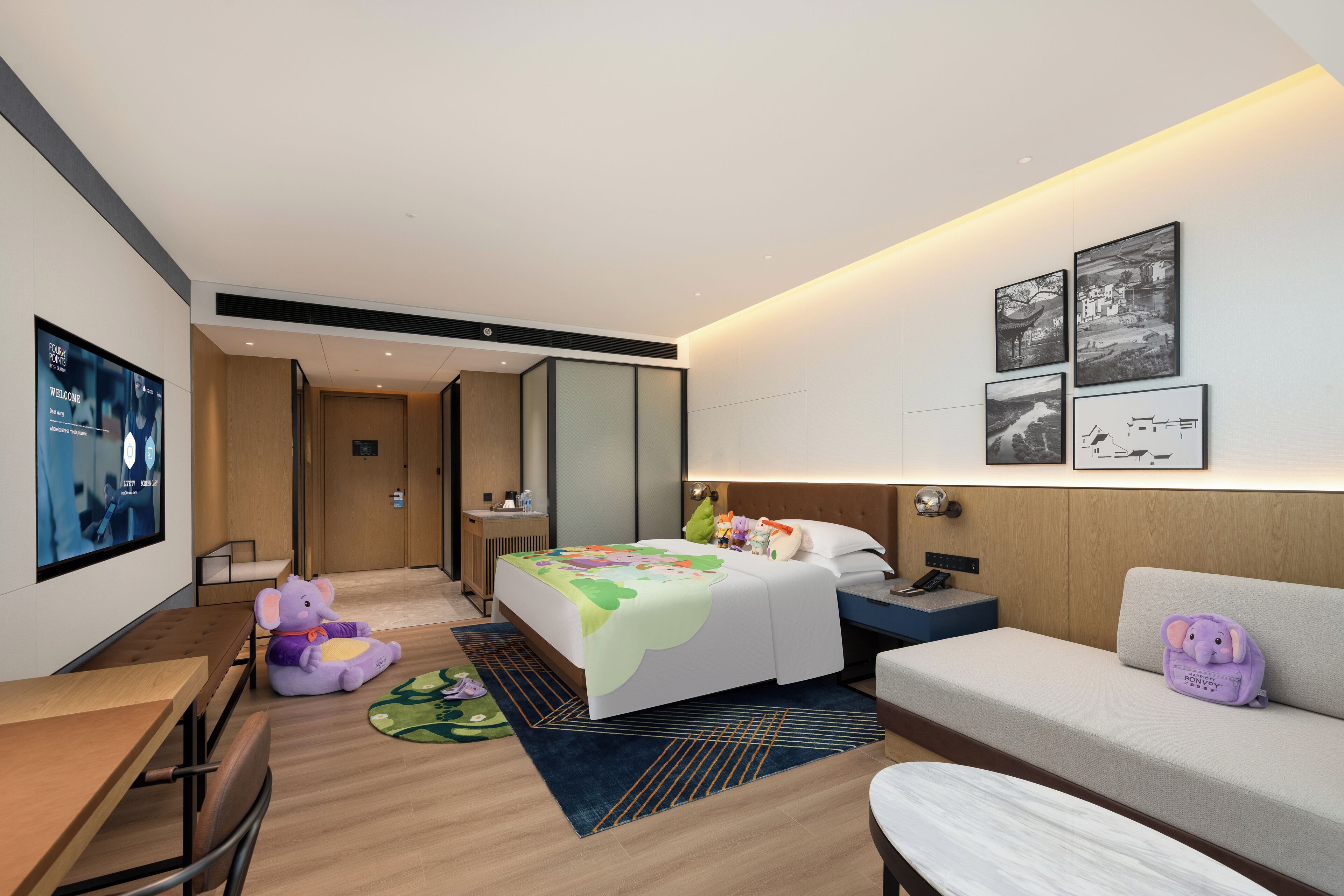 A modern hotel room with a bed, a sofa, a desk, and a TV.