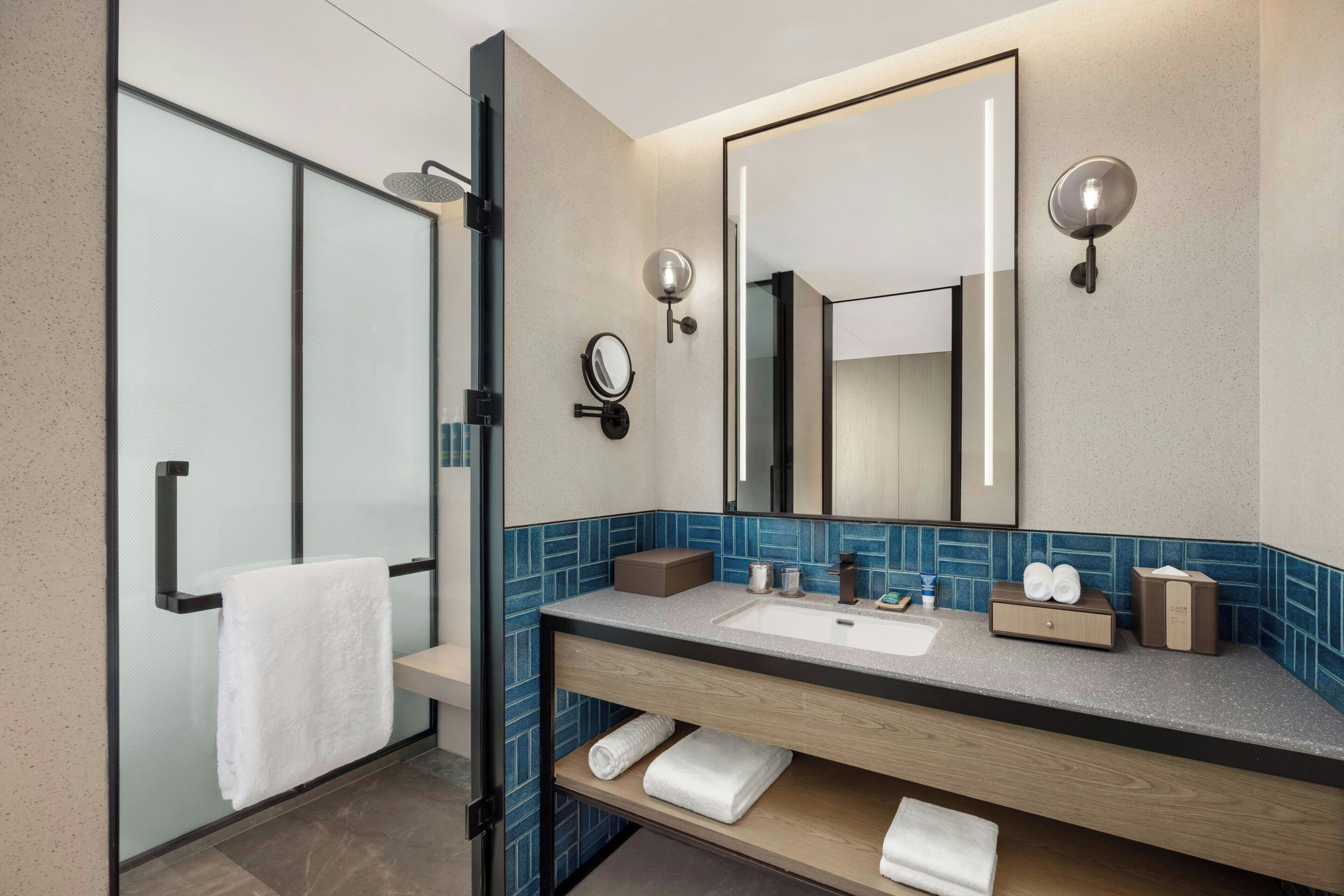 A modern bathroom with a glass shower enclosure, a large mirror, and a vanity with a sink and towel storage.
