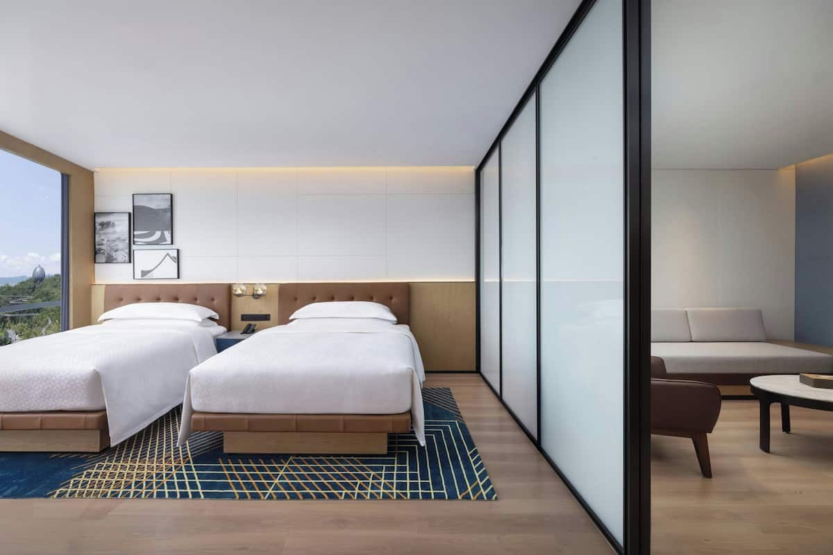 Ein modernes Hotelzimmer mit zwei Betten, einer Couch und Blick auf die Stadt.
