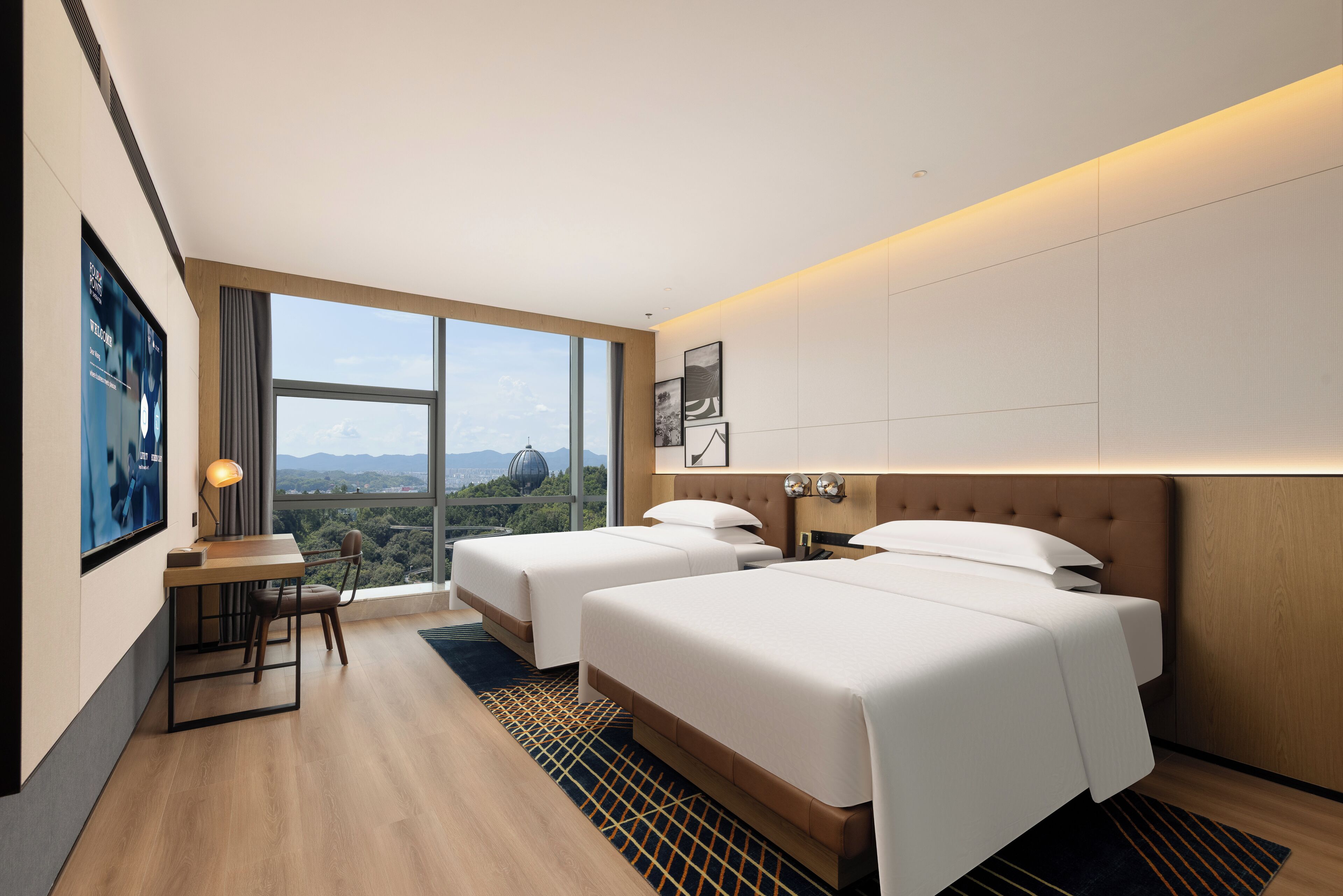 A modern hotel room with two beds, a desk, and a large window offering a city view.