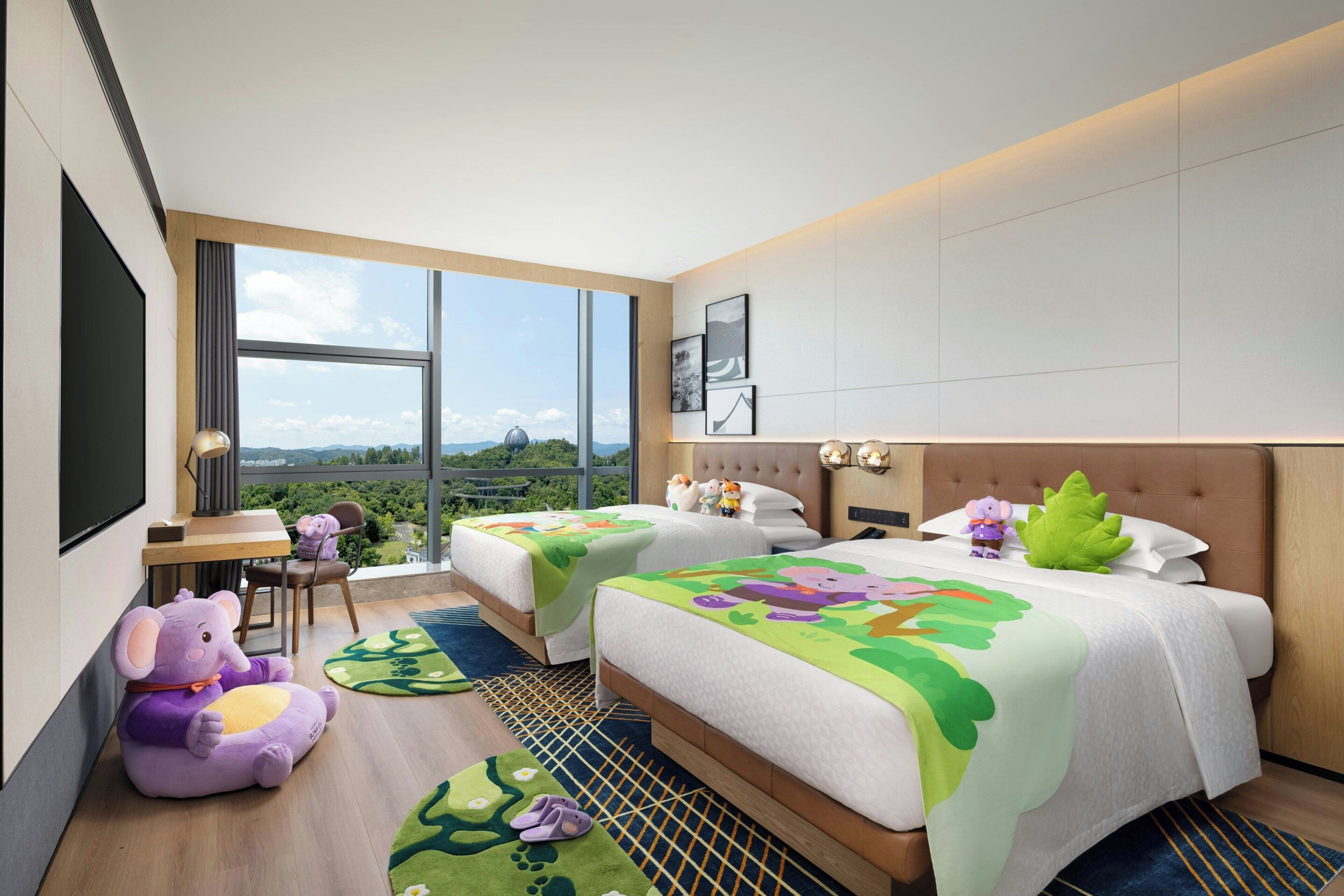 Quarto de hotel com duas camas, uma escrivaninha e uma janela grande com vista para as montanhas.