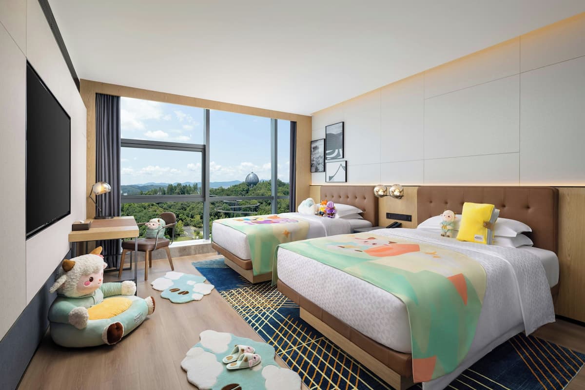 Ein Hotelzimmer mit zwei Betten, einem Schreibtisch und einem großen Fenster mit Blick ins Freie.