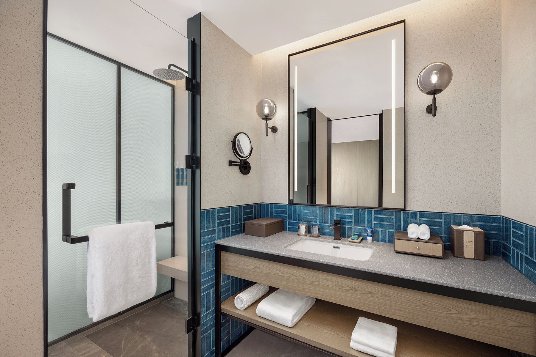 A modern bathroom with a glass shower enclosure, a large mirror, and a vanity with a sink and towel storage.
