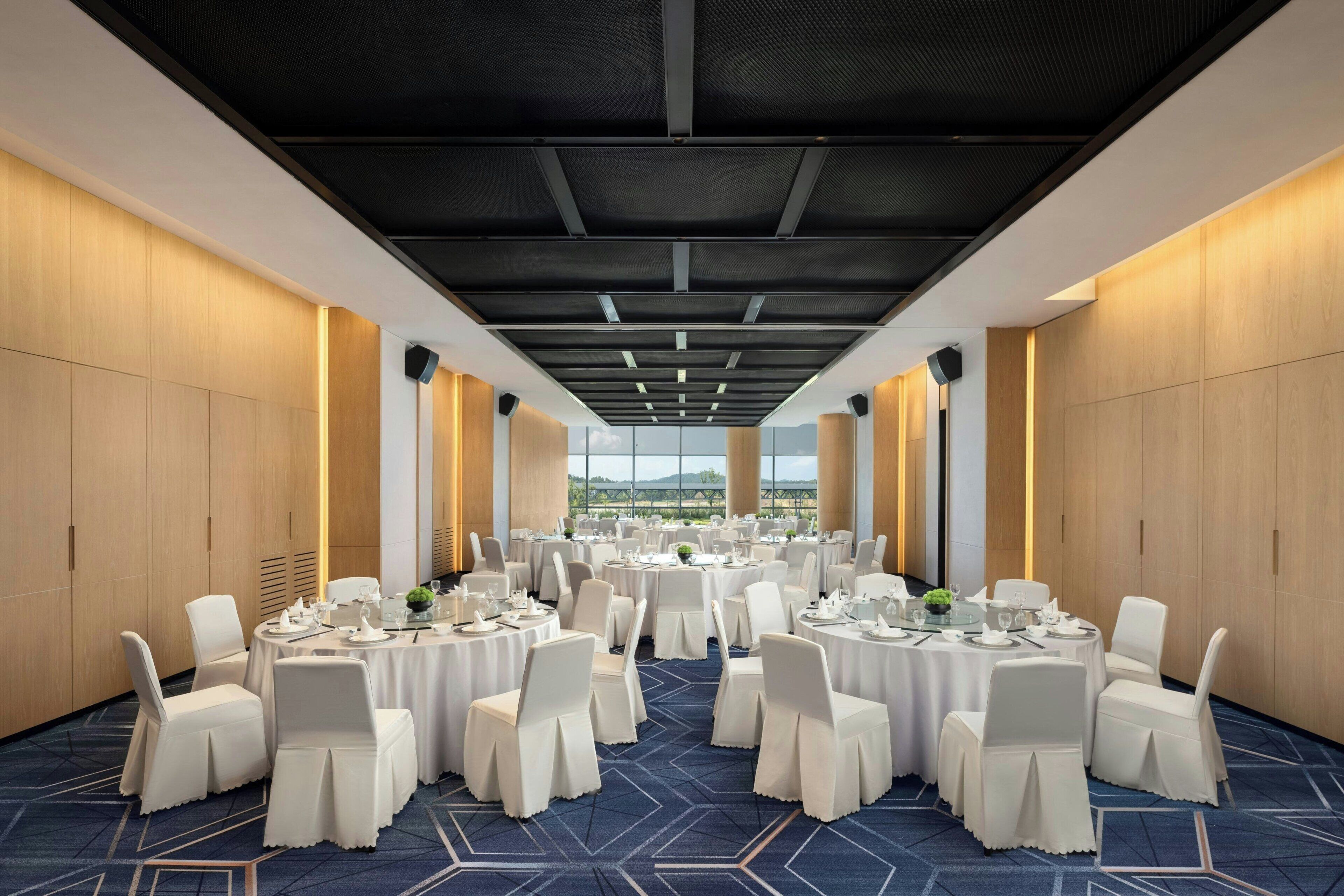 A conference room with round tables and white chairs, large windows, and a high ceiling.