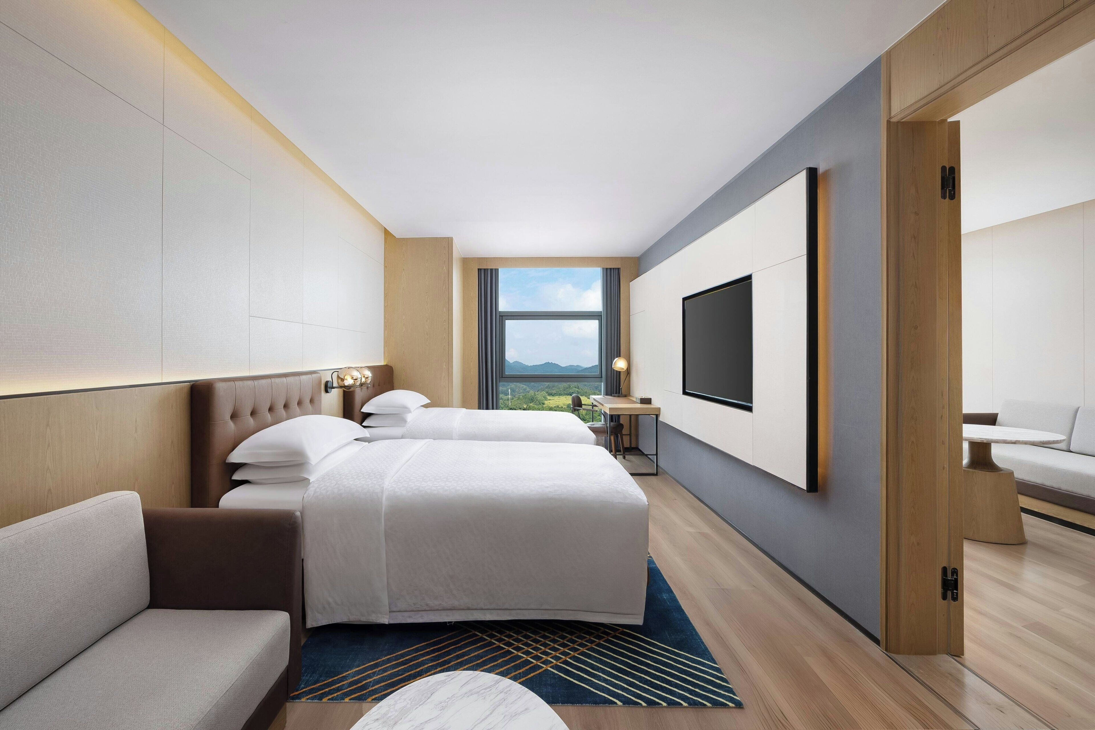 Een moderne hotelkamer met twee bedden, een bank, een bureau en een televisie.