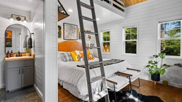 Une chambre avec un lit en mezzanine, une échelle, un bureau et une fenêtre donnant sur un paysage verdoyant.