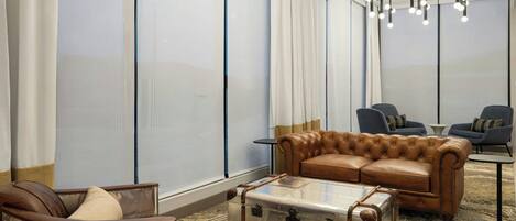Un moderno espacio de lounge con un sofá de cuero, una maleta antigua y un sillón de cuero capitonado.