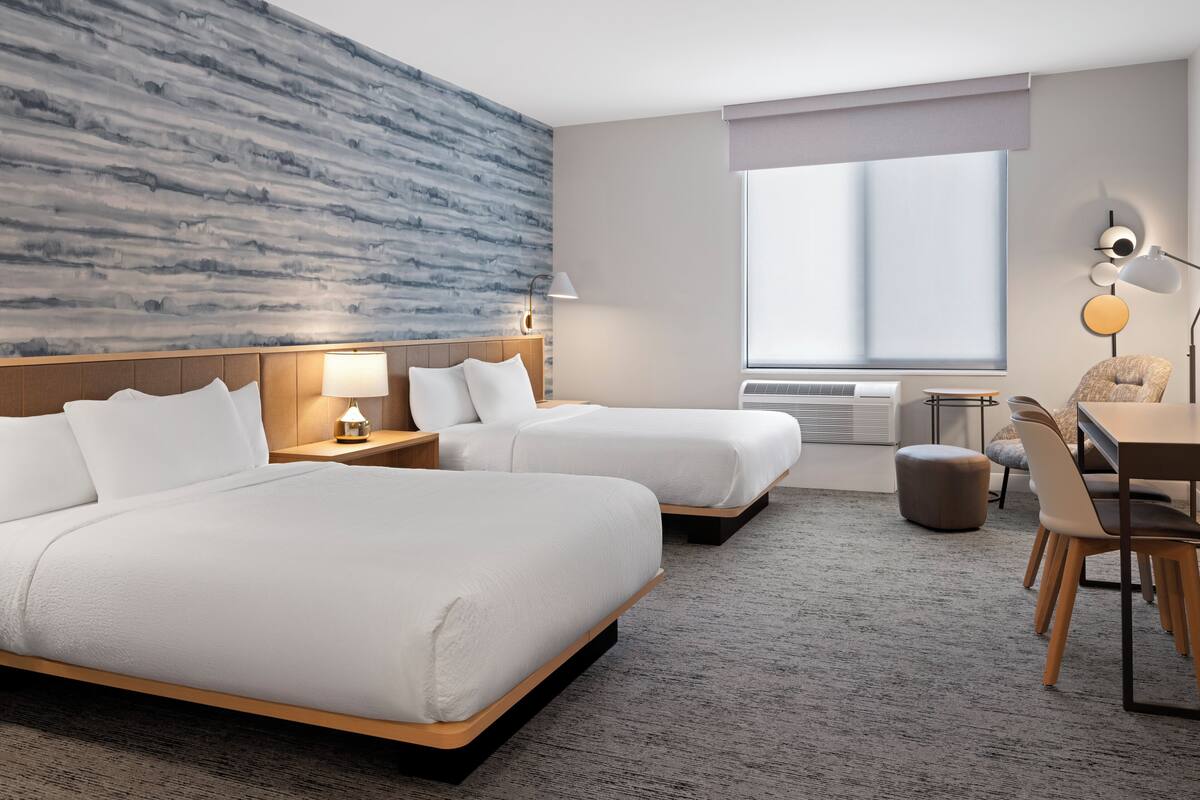 A modern hotel room with two beds, a desk, and a large window.