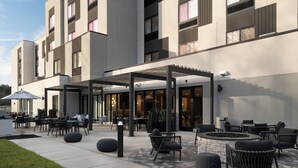 Un bâtiment moderne doté d’un espace extérieur aménagé avec une zone de repos couverte, d’un éclairage extérieur et d’un foyer.