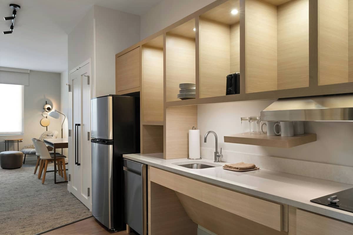 A modern kitchen with a stainless steel refrigerator, wooden cabinets, a built-in oven, and a countertop with a sink and coffee maker.