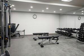 Ein Fitnessraum mit Krafttrainingsgeräten, Bänken und einer Spiegelwand.