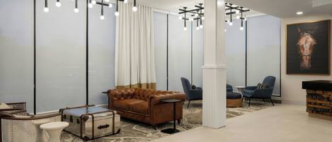 Um lobby moderno com um sofá de couro marrom, duas poltronas azuis, um pilar branco e uma grande pintura de um cavalo.