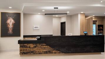A hotel reception area with a modern design, a mounted horse portrait, a reception desk, a digital kiosk, and a minibar.