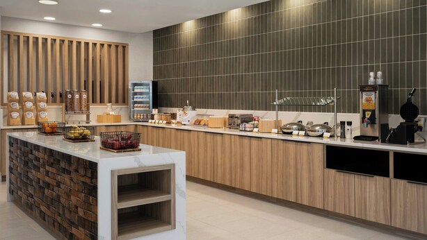 Un café moderne avec un comptoir en marbre, des éléments décoratifs en bois et une grande variété de plats et de boissons au menu.