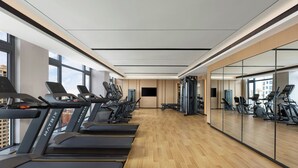 Uma academia com esteiras, bicicletas ergométricas e um espelho grande na parede.
