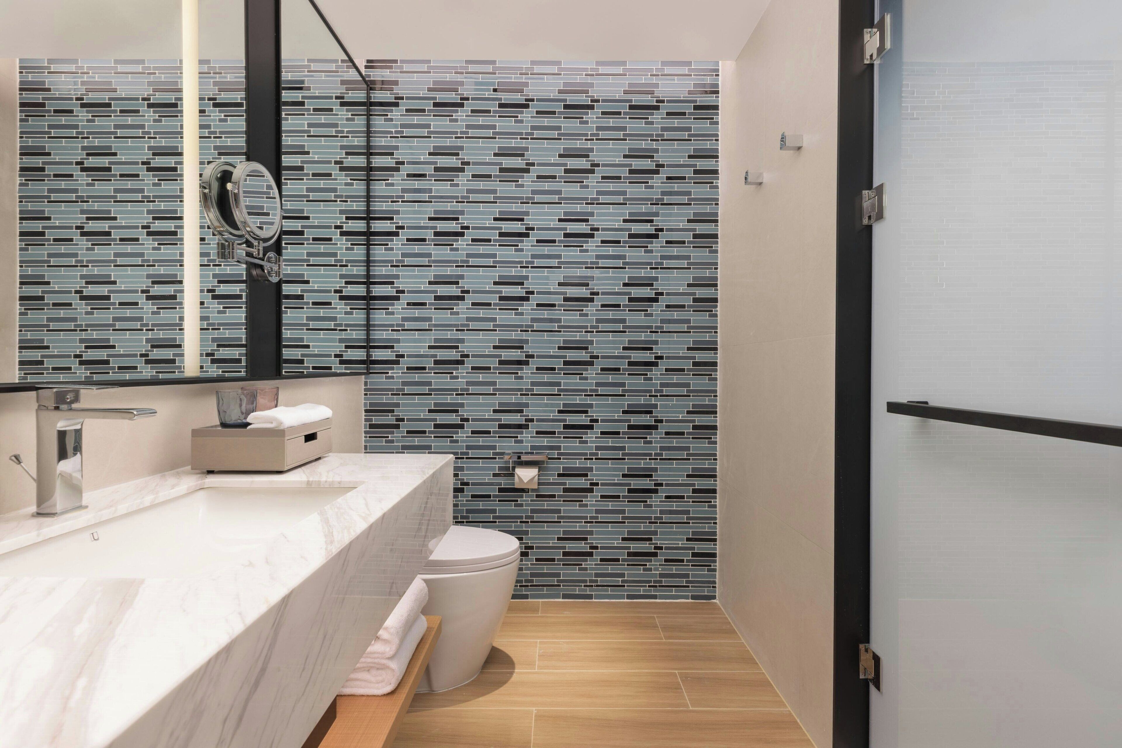 A modern bathroom with a tiled backsplash, a white sink, a toilet, and a mirror.