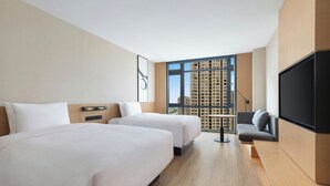 Quarto de hotel com duas camas, um sofá, uma televisão e uma janela grande com vista para a cidade.
