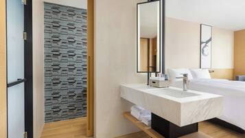 A modern hotel room with a large bed, a marble bathroom sink, and a wooden floor.