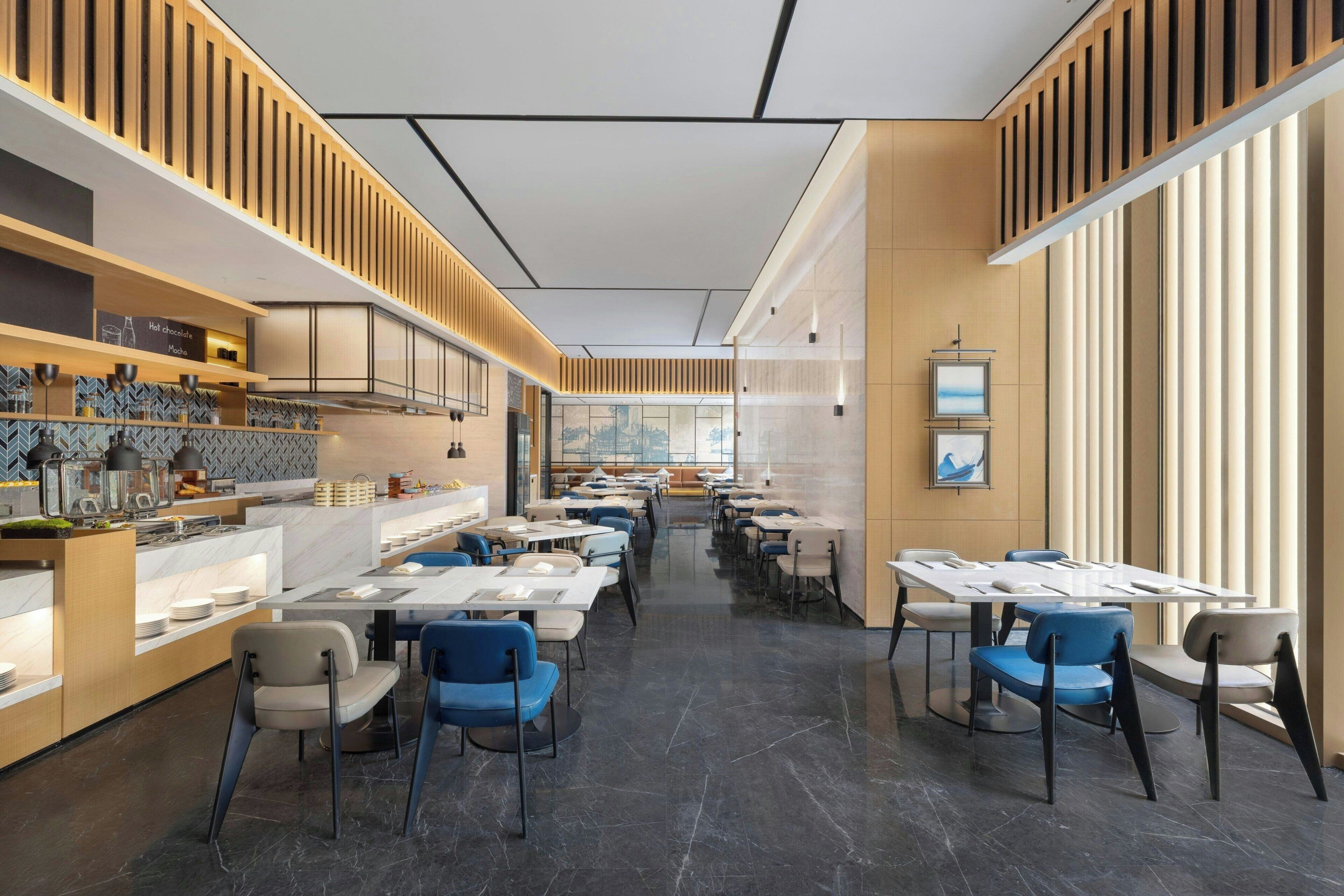A modern restaurant interior with a long counter, seating area, and large windows.