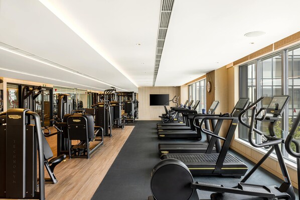 Une salle de sport moderne équipée de tapis de course, d’appareils de musculation et d’un grand miroir.