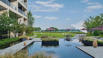 A modern outdoor area with a reflective pool, seating areas, and a building with balconies.