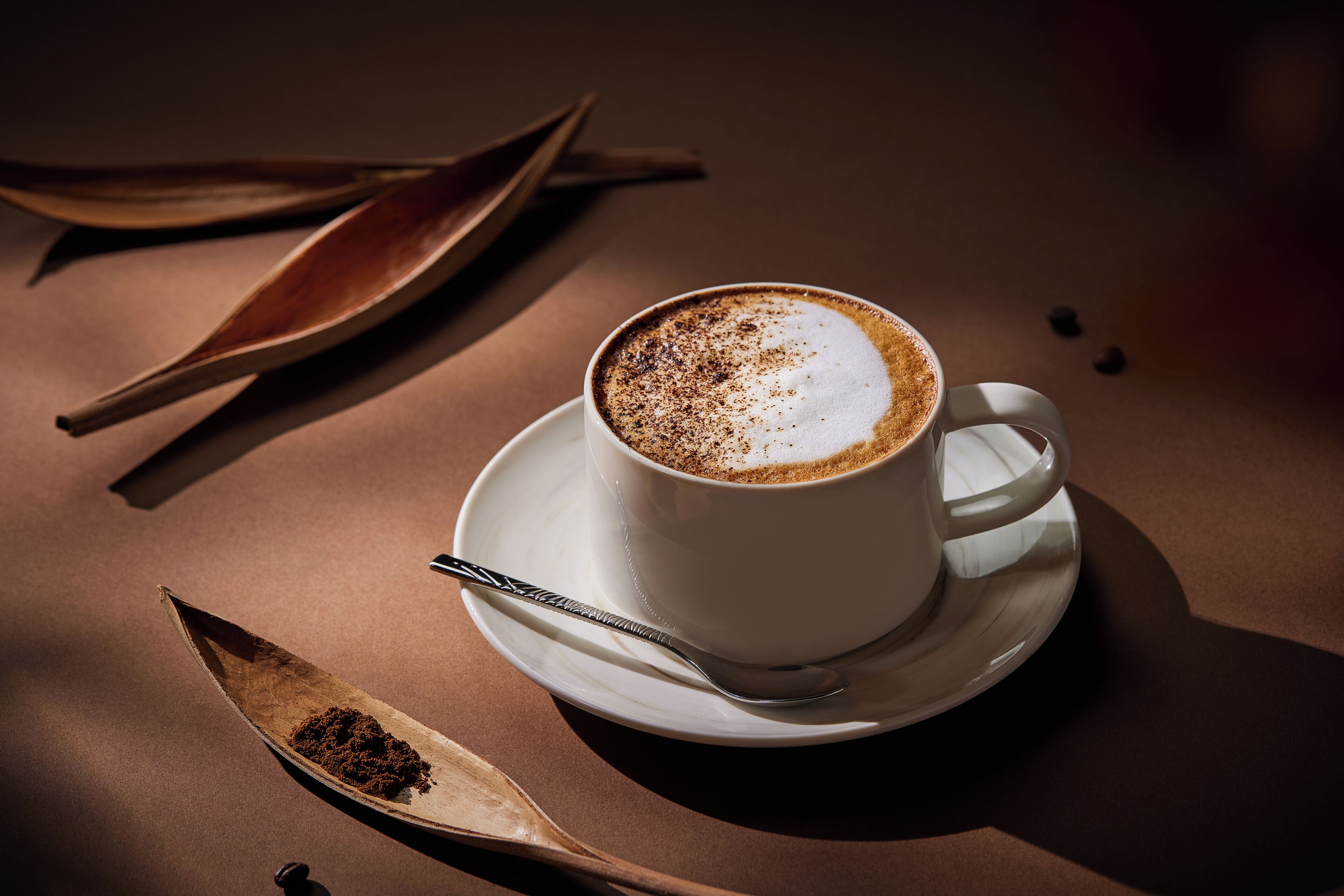 A cup of coffee on a saucer with a spoon and a wooden spoon containing a powdery substance.