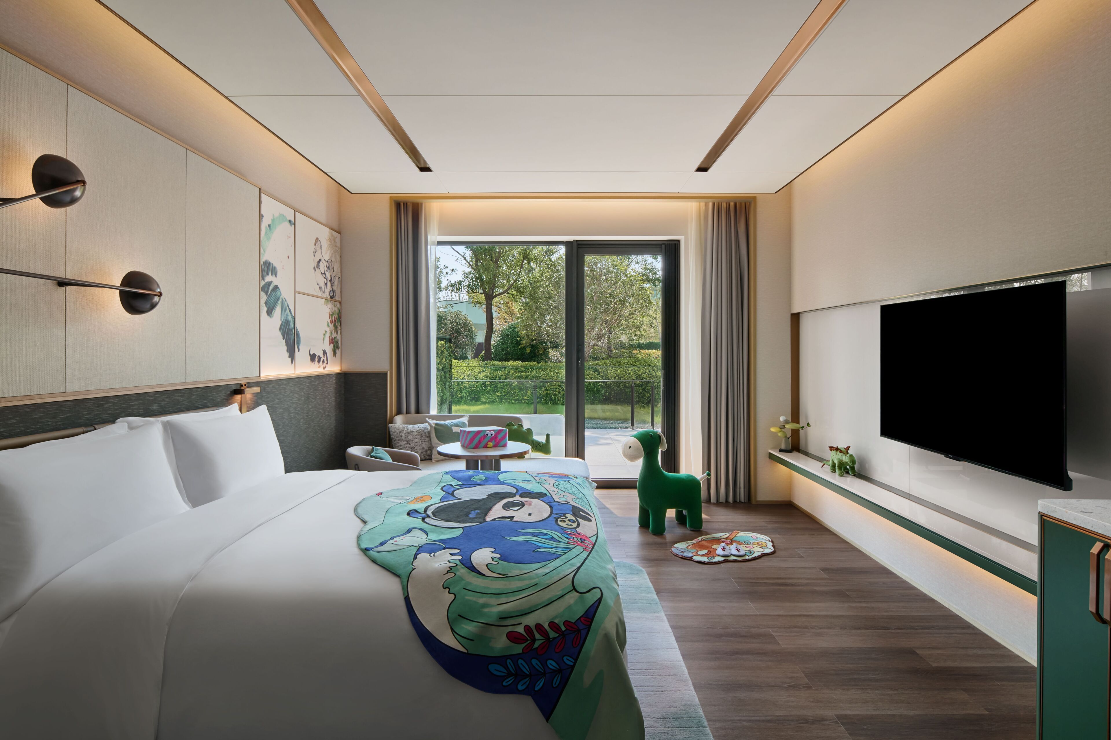 Ein modernes Hotelzimmer mit einem großen Bett, einem Flachbildfernseher, einem Balkon mit Blick ins Grüne und einem kleinen Tisch mit einem Stuhl.
