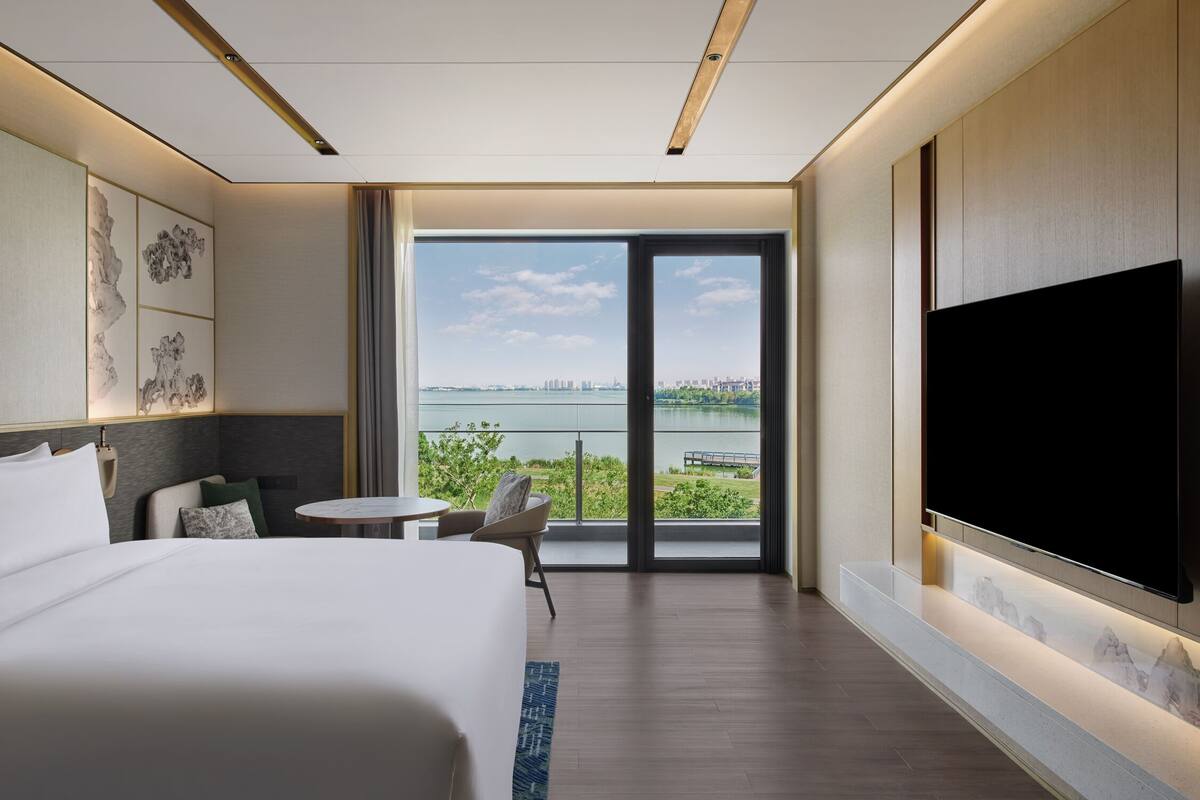 Ein modernes Hotelzimmer mit einem großen Bett, einem Flachbildfernseher, einem Balkon mit Stadtblick und einem Essbereich.