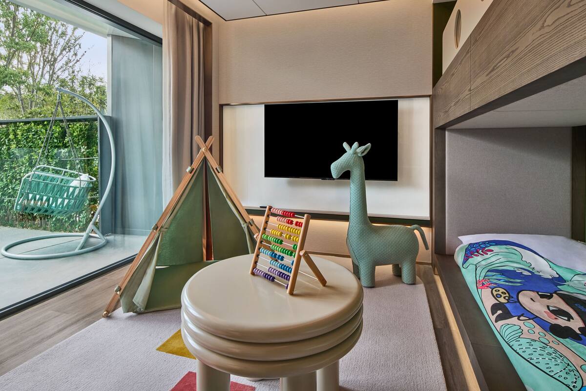 Ein Zimmer mit einem Etagenbett, einem Fernseher, einem Hängesessel und einem kleinen Tisch mit einem bunten Rechen.
